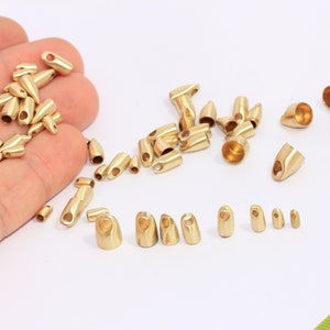 Può includere: Una collezione di cappucci terminali in metallo dorato per cordini o la creazione di gioielli. I cappucci terminali sono di varie dimensioni e forme, alcuni con un'apertura a forma di anello.