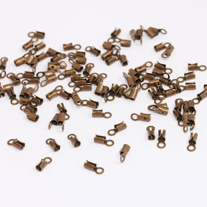 May include: A large quantity of small, gold-toned metal crimp beads. The beads have a small loop on one end and a crimping section on the other end.