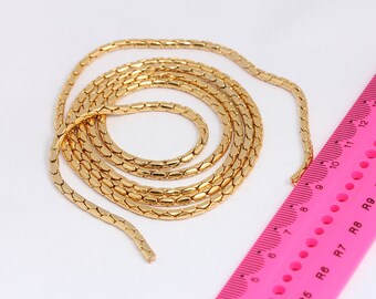 May include: A gold chain necklace with a snake chain design. The chain is approximately 12 inches long and is measured against a pink ruler.