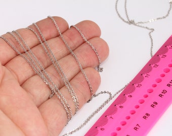 May include: A silver chain necklace measuring 15 inches long, laid out on a hand and a pink ruler. The ruler has markings for inches and centimeters.