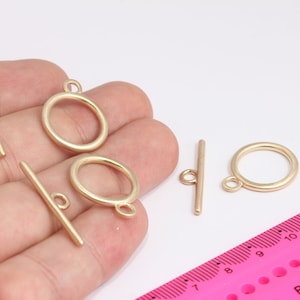Könnte beinhalten: Goldfarbene Metall-Schiebeverschlüsse mit runden Ringen. Es gibt insgesamt vier Verschlüsse, zwei mit Ringen und zwei ohne.