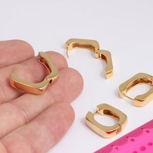 May include: Three pairs of gold hoop earrings. The earrings are all different shapes and sizes. The earrings are on a white surface.