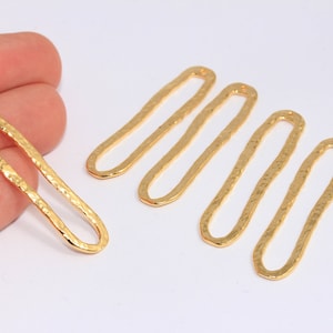 Peut inclure: Cinq breloques ovales en métal doré avec une texture martelée. Chaque breloque a un trou en haut pour l'attacher à des bijoux.