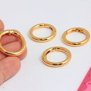 May include: Four gold-coloured metal rings with a spring-loaded clasp. The rings are approximately 2.5 cm in diameter.