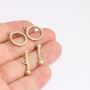 May include: Three gold-toned metal jewelry findings. Two are round, open-ended rings with a hammered texture. One is a straight bar with rounded ends and a loop in the center.