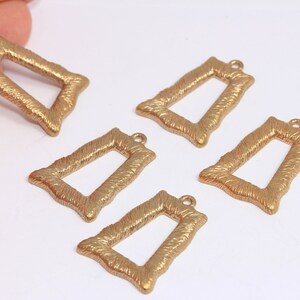 May include: Five gold-toned metal picture frame charms with a textured surface. The charms are rectangular with a small loop at the top for attaching to a necklace or bracelet.