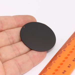 Puede incluir: Un círculo de metal negro con un pequeño agujero en el centro. El círculo tiene un diámetro de aproximadamente 5 cm.