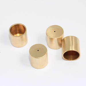 Op de afbeelding: Vier gouden metalen kaarsenhouders met een klein gaatje bovenaan. De kaarsenhouders zijn cilindrisch van vorm en hebben een gladde, gepolijste afwerking.