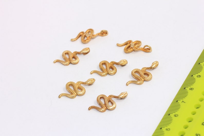 May include: Seven gold-colored snake charms, each with a detailed, textured design. The charms are scattered on a white surface.