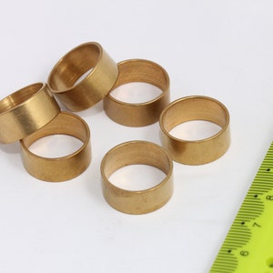 Op de afbeelding: Zes gouden metalen ringen in verschillende maten, gerangschikt op een wit oppervlak. Een groene liniaal met zwarte markeringen is zichtbaar op de achtergrond.
