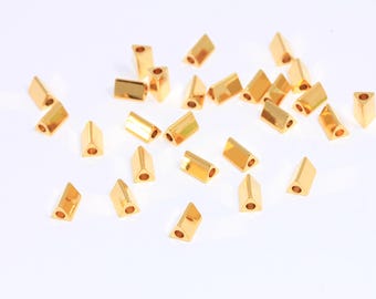 May include: A group of gold-colored triangle-shaped beads with a hole in the center. The beads are scattered on a white surface.