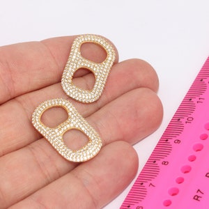Op de afbeelding: Twee goudkleurige metalen bedels met een dubbele ringvorm, elke bedel is volledig bezet met kleine, heldere strass steentjes.