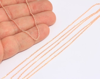 May include: Close-up of several delicate rose gold necklaces. The chains are thin and have a subtle sparkle, lying against a white background. The necklaces are displayed in a hand, showcasing their length and design.