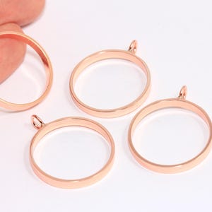 May include: Four rose gold-colored pendant blanks with a circular design. Each blank has a small loop at the top for attaching a chain or cord. The pendants are displayed on a white surface.