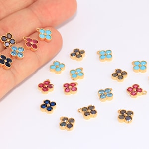 Peut inclure: Assortiment de breloques en forme de fleur dorées avec des pierres précieuses de différentes couleurs. Les breloques présentent un motif de fleur à quatre pétales avec une boucle pour les attacher à des bijoux.