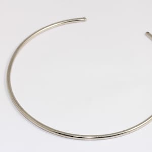 May include: A silver choker necklace made of a single, thin, round piece of metal.