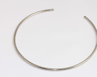 May include: A silver choker necklace made of a single, thin, round piece of metal.