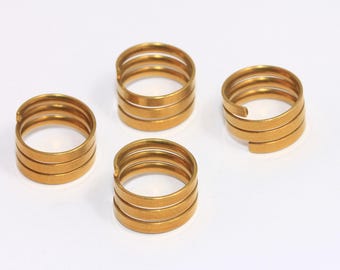 Puede incluir: Cuatro anillos de metal de color dorado, cada uno con tres espirales. Los anillos están dispuestos en semicírculo sobre una superficie blanca.