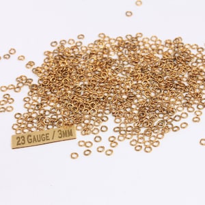 Könnte beinhalten: Ein großer Haufen goldener Sprungringe mit einem Durchmesser von 3 mm und einem Etikett mit der Aufschrift "23 Gauge / 3MM".