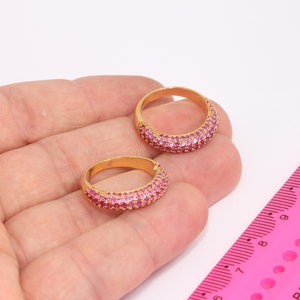 Peut inclure: Deux bagues en or avec des pierres roses serties dans une bande. Les bagues sont sur une main, et une règle rose est en arrière-plan.