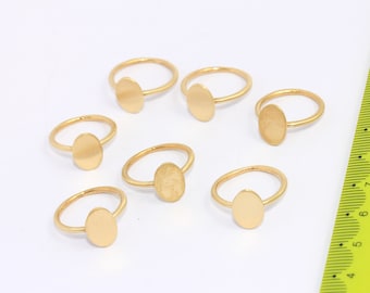 Puede incluir: Siete anillos de oro con tapas de forma ovalada. Los anillos están dispuestos sobre una superficie blanca junto a una regla amarilla.