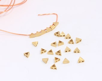 May include: A collection of gold triangle beads with two holes in each. Some beads are strung on a copper wire.