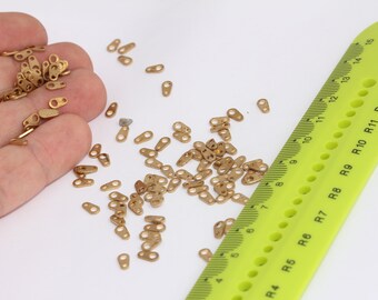 May include: A large pile of small, gold-coloured metal loops or rings. A green ruler with black markings and the text "Y-PLUS" is visible in the background.