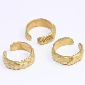 May include: Three gold-toned rings with a textured surface. The rings are open and have a slightly curved shape.