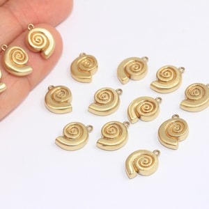 Puede incluir: Una colección de 14 dijes de concha marina de metal dorado. Cada dije presenta un diseño en espiral detallado.