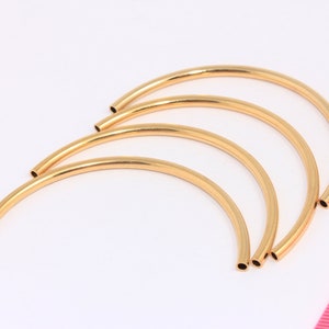 May include: Four gold-coloured metal hoops, each with a slightly different diameter, are arranged in a stack. The hoops are open on both ends and have a smooth, polished finish.