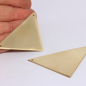 Peut inclure: Deux pendentifs en métal de forme triangulaire de couleur dorée avec des trous pour la suspension.
