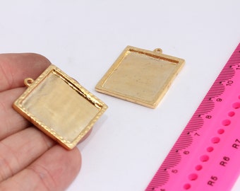 May include: Two gold-coloured metal picture frames with a decorative border. The frames are square and have a loop at the top for hanging. The frames are on a white surface.
