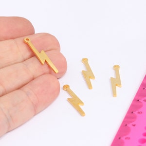 May include: Four gold-colored lightning bolt charms with a small loop at the top. The charms are about 1.5 inches long and are arranged on a white surface.
