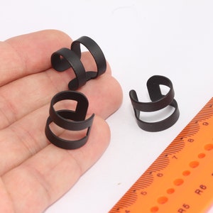 May include: Three black metal ear cuffs. The cuffs are made of two rings, one larger than the other, that are connected by a spring.