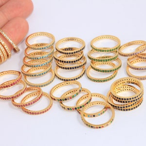 Puede incluir: Una colección de anillos dorados con piedras preciosas de colores. Los anillos están apilados y dispuestos sobre una superficie blanca.