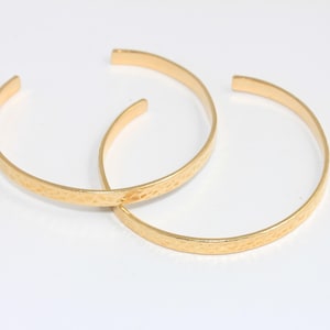 Op de afbeelding: Twee gouden, gehamerde metalen armbandjes. De armbandjes liggen op elkaar.