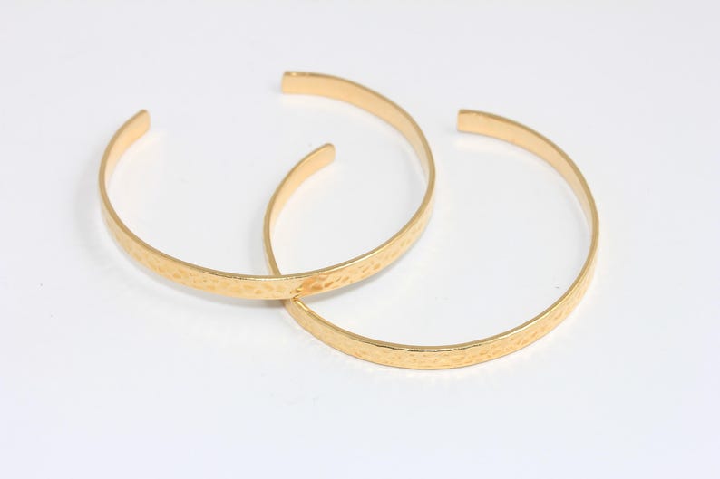 Op de afbeelding: Twee gouden, gehamerde metalen armbandjes. De armbandjes liggen op elkaar.