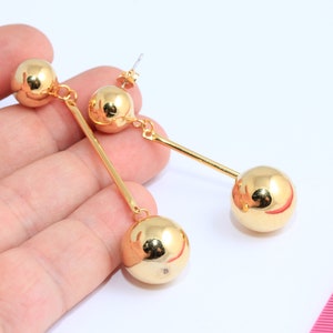 May include: A pair of gold-tone dangle earrings with two round balls on each earring. The earrings are approximately 2 inches long.