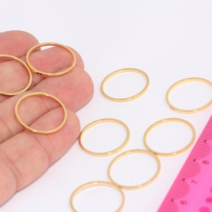 Op de afbeelding: Acht gouden metalen ringen in verschillende maten, uitgelegd op een wit oppervlak. Een roze liniaal met zwarte markeringen is zichtbaar in de rechterbenedenhoek van de afbeelding.