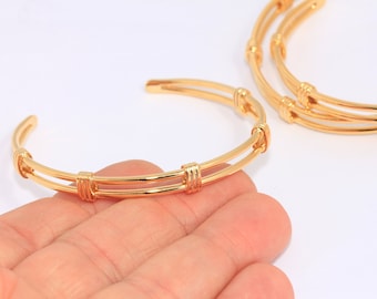 May include: Two gold-toned bangle bracelets with a simple, woven design. The bracelets are stacked on top of each other.