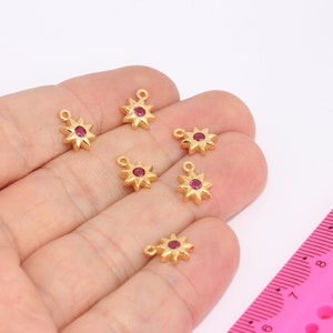 May include: Six gold-toned star-shaped charms with a red rhinestone in the center. The charms have a loop at the top for attaching to jewelry.