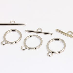 May include: Five silver-toned metal toggle clasps for jewelry making. Three are round with a small loop on the side. Two are straight bars with a loop at one end.