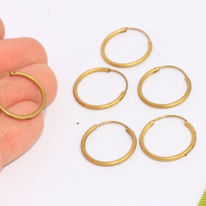 Peut inclure: Cinq boucles d'oreilles créoles en or, chacune d'un diamètre d'environ 2,5 cm. Les boucles d'oreilles sont disposées en demi-cercle sur une surface blanche.