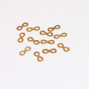 Könnte beinhalten: Eine Streuung von goldfarbenen Unendlichkeits-Anhängern auf weißem Hintergrund.