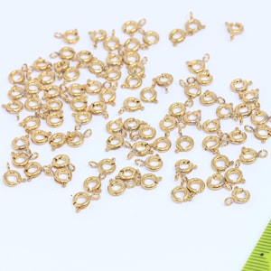 Puede incluir: Una gran cantidad de anillos de salto de metal dorado. Los anillos son pequeños y circulares, con un mecanismo de cierre.