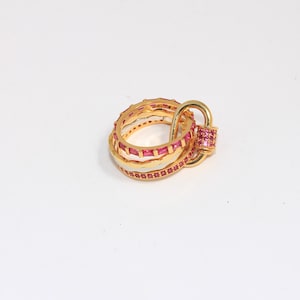 Pode incluir: Conjunto de três anéis de ouro, cada um adornado com pedras de zircônia cúbica rosa. A banda superior apresenta um design único de laço aberto.
