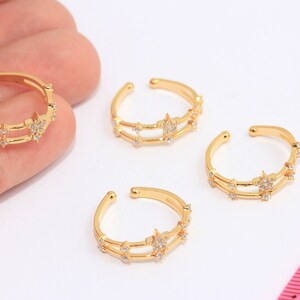 May include: Three gold-toned adjustable rings with a double band design. Each ring is adorned with small, clear cubic zirconia stones arranged in a star shape.