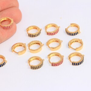 May include: Assortment of gold hoop earrings with colourful cubic zirconia stones. The earrings are available in blue, pink and red.