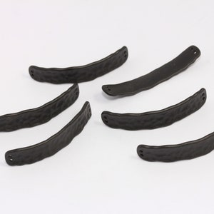 Puede incluir: Seis piezas de herrajes de metal negro con textura martillada. Cada pieza tiene dos agujeros y tiene forma de barra curva.