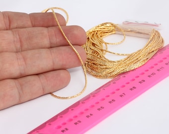 May include: A close-up of a gold chain, measuring 13 inches long, with a textured surface. The chain is coiled and laid on a pink ruler with markings for inches and ring sizes.